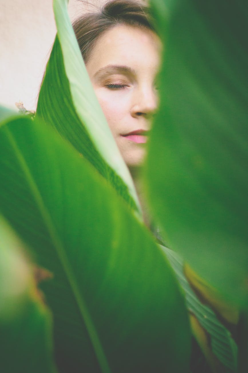 woman closing her eyes at the back of green leaves
